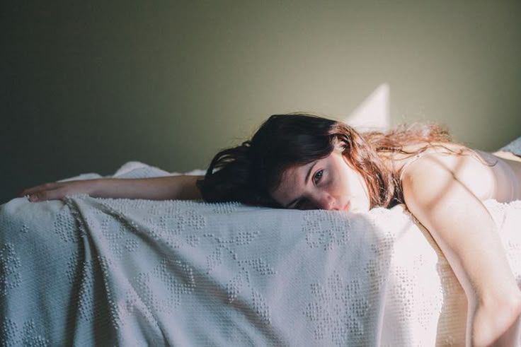 A woman looking defeated and laying face down on her bed.